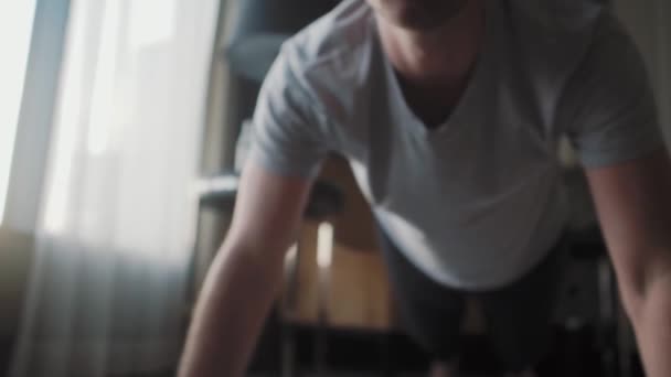 En man i hemkläder trycks ner från golvet. Han idrottar hemma. — Stockvideo