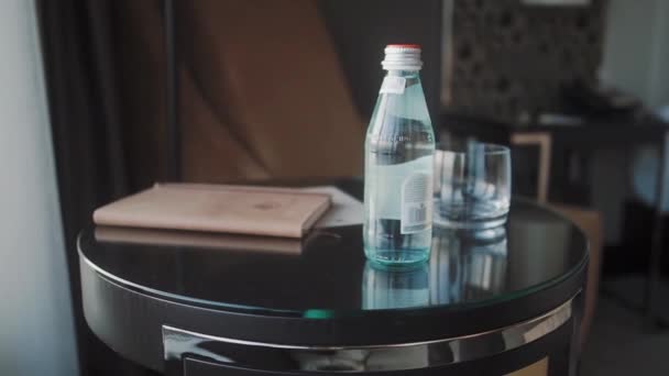 Ein Mann nimmt eine Glasflasche Wasser vom Tisch. — Stockvideo