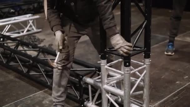 A worker assembles a metal structure on stage — Stockvideo