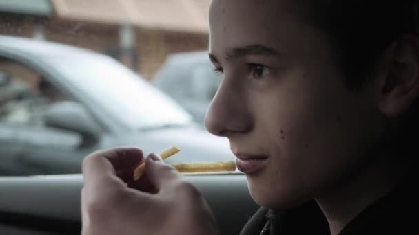 Teenager sedí v autě a jí hranolky — Stock video