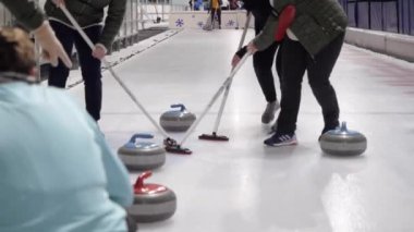 Kadınlar arenada curling oynarlar.