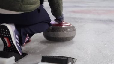 Bir kadın Curling oynuyor. Buzda kayıyor.
