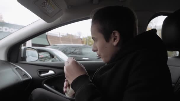 Teen boy sits on front seat of car and eats ice cream — Stock Video