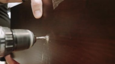 Bir matkap, ahşap mobilya cephesinde delik açıyor.