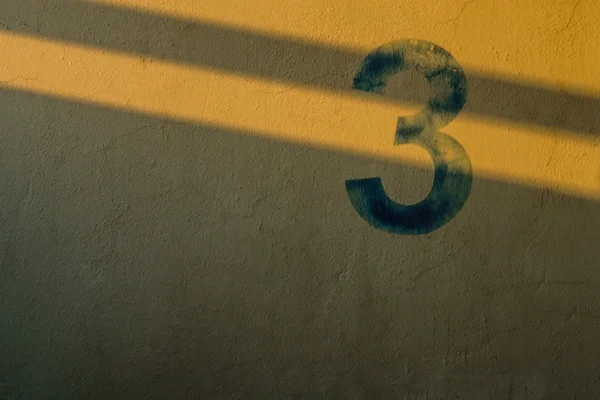 O número 3 na parede sob a sombra das luzes — Fotografia de Stock