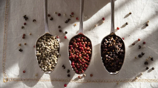 Different peppers and pink berries in spoons