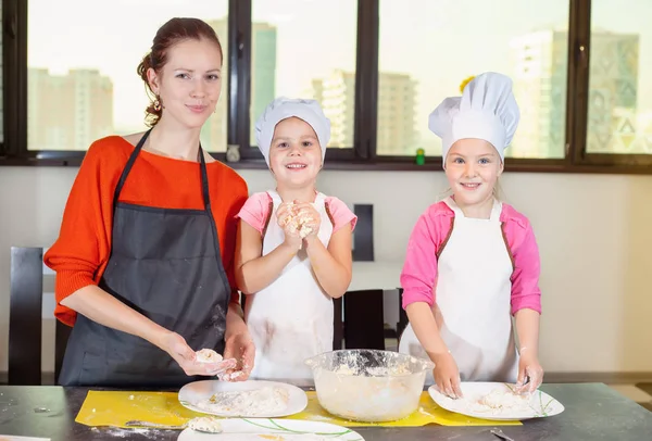 Dos niños encantadores junto con la madre preparando un pastel — Foto de Stock