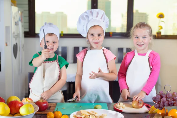 Tres niños lindos están preparando una ensalada de frutas en la cocina — Foto de Stock