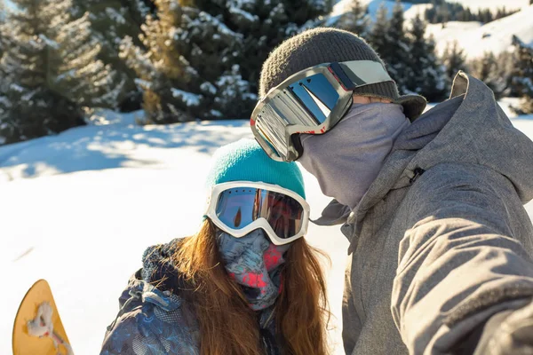 Para snowboardzista, stojąc na szczycie góry o zachodzie słońca i podejmowania selfie — Zdjęcie stockowe