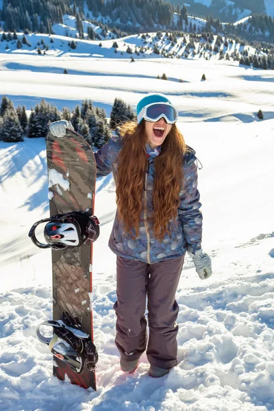 Дівчина сноубордист стоїть на вершині гори зі сноубордом в руках . — стокове фото