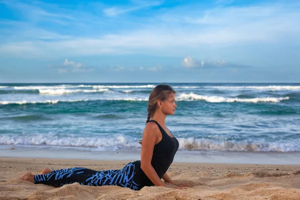 Jeune femme pratiquant le yoga sur la plage au lever du soleil — Photo