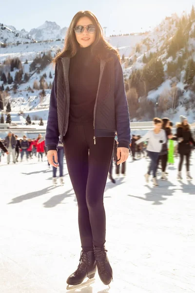 Jolie femme patinant sur glace l'hiver à l'extérieur, sourire au visage. Montagnes en arrière-plan Photo De Stock