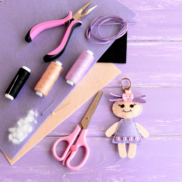 Creative art and craft idea for kids. Felt doll keychain, scissors, thread, needles, pins, suede cord, pliers, felt sheets on wooden background. Set to create kids keychain. Top view — Stock Photo, Image