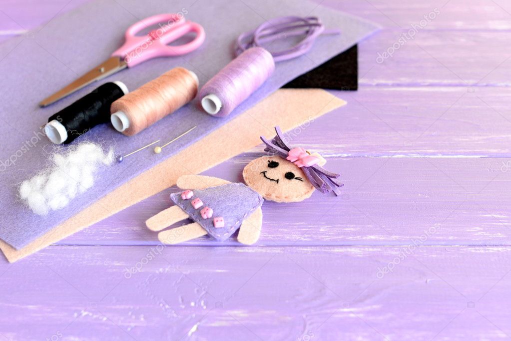 Creative art and craft idea for children. Felt doll, scissors, thread,  needles, pins, suede cord, felt sheets on wooden background with empty  place for text. Set to create children toy Stock Photo