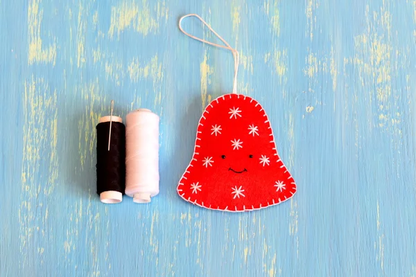 How to sew a Christmas felt bell ornament. Step. Fun felt Christmas bell ornament, white and black threads on a blue wooden background. Home decor idea for children. Easy felt sewing diy. Top view — Φωτογραφία Αρχείου