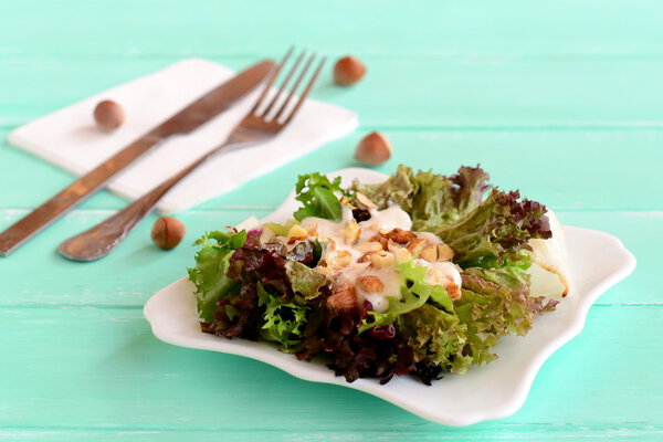 Fresh salad leaves with yogurt and nuts on a plate. Salad is prepared from radicchio, lettuce, iceberg, frieze. Diet food recipe. Fork, knife on a wooden background. Closeup 