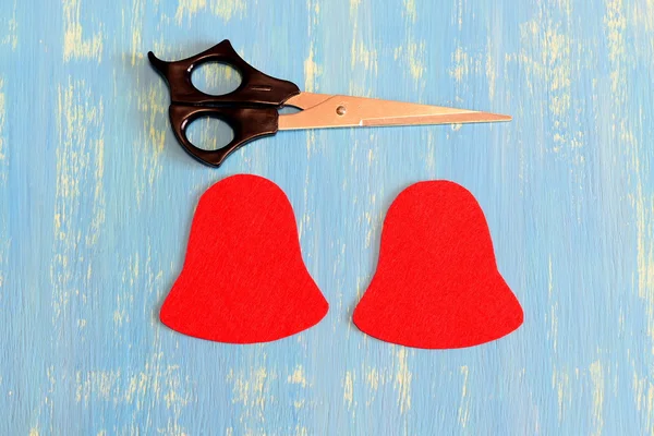 How to make a Christmas bell decor. Step. Cut felt parts to create a Christmas tree decor. Red felt bell patterns, scissors on wooden background. New year's sewing kit. Top view — Stockfoto