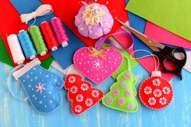 Yılbaşı ağacı süsleri el sanatları. Pembe Keçe kalp, kırmızı ve yeşil Noel ağacı, mavi mitten, kırmızı top ahşap arka plan üzerinde. Dikiş malzemeleri, iş parçacığı, makas, iğne, keçe sayfaları, iğnelik, iğne 