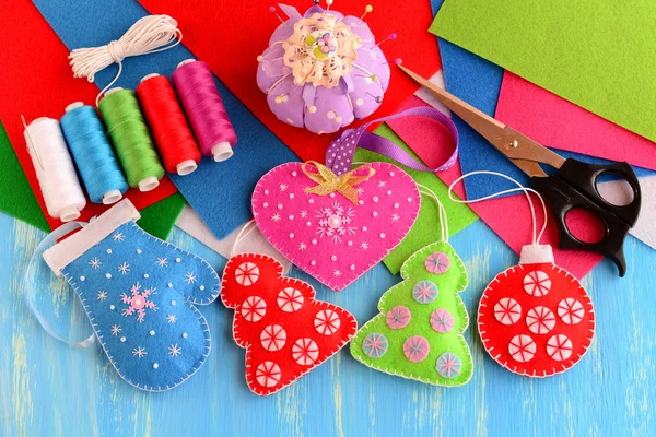 Christmas tree decorations crafts. Felt pink heart, red and green Christmas tree, blue mitten, red ball on wooden background. Sewing supplies, thread, scissors, needle, felt sheets, pincushion, pins — Stock fotografie