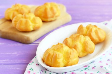 Lezzetli tatlı eklerleri veya kremalı profiterol. Ev yapımı tereyağı bir plaka ve ahşap kesme tahtası üzerinde krema dolu eklerleri. Portre 