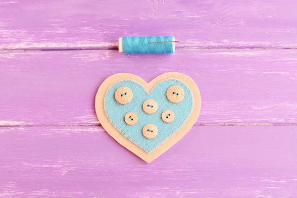How to sew a felt heart decor. Step. Sew buttons with a blue thread on one side of a felt heart. Blue thread, needle on wooden background. Souvenir for Valentine's day, wedding, mother's day — Stock Photo, Image