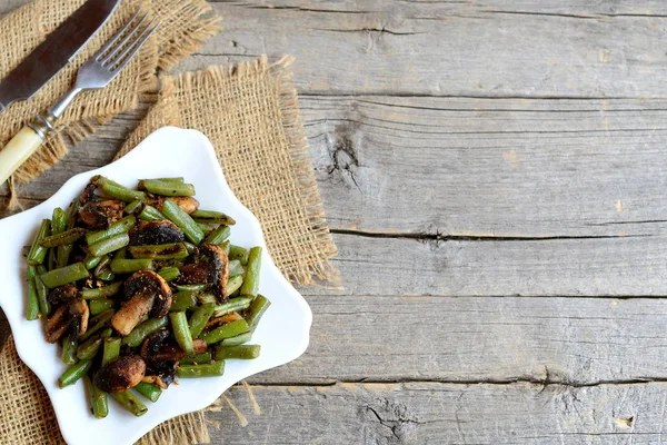 Haricots verts frits épicés avec champignons sur une assiette et sur un vieux fond en bois avec copie espace vide pour le texte. Recette de salade de haricots verts chauds et champignons. Style vintage. Vue du dessus — Photo