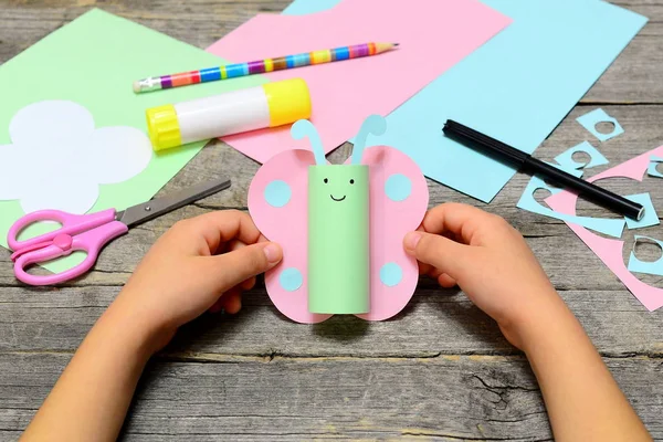 Enfant tenant du papier artisanat papillon dans les mains. Enfant montre un artisanat de papier amusant. Papeterie sur une vieille table en bois. Art du papier d'été préscolaire et maternelle. Bricolage facile pour les enfants — Photo