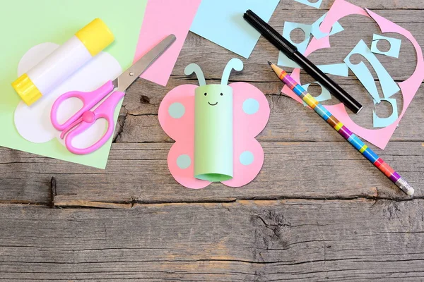 Funny pastel paper butterfly, scissors, marker, glue stick, colored paper sheets and scraps, pencil on old wooden table. Children craft activities workplace. Summer kids art craft project in kindergarten, camp or home. Kids minimal handmade concept — Stock Photo, Image