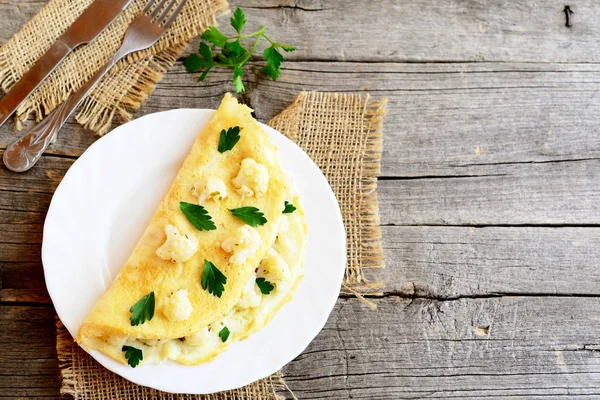 Tortilla de coliflor decorada con perejil. Tortilla vegetariana con relleno de coliflor en un plato, tenedor y cuchillo sobre fondo de madera vieja con espacio en blanco para texto. Estilo vintage. Cocina casera simple —  Fotos de Stock