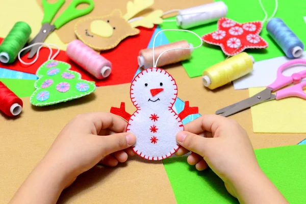 Criança pequena segurando um boneco de neve de Natal sentido em mãos. Criança mostra artesanato ornamento de Natal. Local de trabalho no jardim de infância, escola ou casa. Crianças artesanato de Natal ideia. Crianças inverno criatividade — Fotografia de Stock