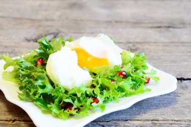 Haşlanmış yumurta, zeytin yağı ile nar taneleri frise marul yaprakları. Bir plaka üzerinde sağlıklı salata eski ahşap arka plan izole. Lezzetli Yumurta tarifi. Portre 