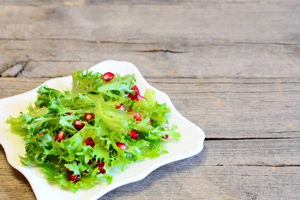 Hojas de lechuga fresca con semillas de granada vestidas con jugo de limón y aceite de oliva. Receta de ensalada simple brillante. Ensalada vegetariana dieta en un plato sobre fondo de madera con lugar en blanco para el texto — Foto de Stock