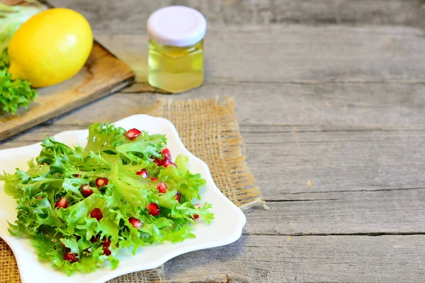 Lechuga fresca con granada aderezada con jugo de limón y aceite de oliva. Brillante comida vegetariana fácil. Ensalada saludable en un plato, ingredientes, tenedor, cuchillo sobre fondo de madera con lugar de copia para el texto — Foto de Stock