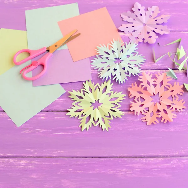 Πολύχρωμο χαρτί νιφάδες χιονιού στολίδια, χρωματιστά φύλλα χαρτιού και παλιοσίδερα, ψαλίδι σε λιλά ξύλινο φόντο. Κάνοντας τα Χριστούγεννα αποκόμματα νιφάδες χιονιού από χρωματιστό χαρτί. Χειμερινές χειροτεχνίες για παιδιά. Καλές κινητικές δραστηριότητες για παιδιά προσχολικής ηλικίας — Φωτογραφία Αρχείου