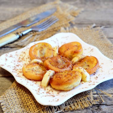 Kızarmış muz börek çikolata ile dekore edilmiş ve taze dilimlenmiş muz. Kolay lezzetli kızarmış muz meyilli bir tabak, çatal, bıçak, çuval bezi üzerinde ahşap masa üzerinde bulunmaktadır. Vejetaryen kahvaltı tarifi. Portre 