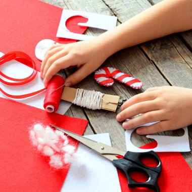 Çocuklar ellerinde eski ahşap masa. El yapımı keçe Noel candy süsleme, keçe çarşafları ve hurda, makas, kırmızı iplik, iğne, kağıt şablonu, pin. Bebek işyeri. Çocuklar Noel sanat projesi 