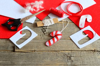 Keçe Noel şeker kamışı süsleme, makas, kağıt şablonu, iş parçacığı, iğne, kırmızı ve beyaz keçe parçaları ve artıkları, dolgu, eski ahşap arka plan üzerinde şerit. Noel DIY kavramı. Çocuklar tatil el sanatları 