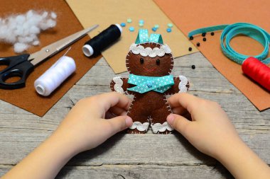 Bir sevimli gingerbread adam süs onun elinde tutan çocuk. Noel ağacı zencefilli kurabiye adam süsleme, el sanatları malzemeleri eski ahşap masa üzerinde. Çocuklar için Noel DIY hissettim. Ev yapımı dikiş kavramı 