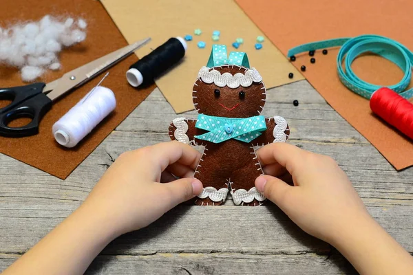 Bir sevimli gingerbread adam süs onun elinde tutan çocuk. Noel ağacı zencefilli kurabiye adam süsleme, el sanatları malzemeleri eski ahşap masa üzerinde. Çocuklar için Noel DIY hissettim. Ev yapımı dikiş kavramı 