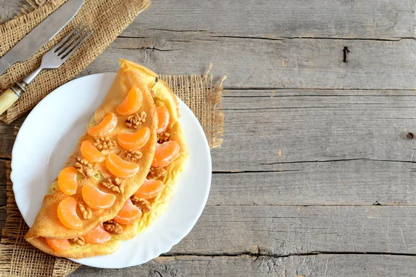 Omelete crocante em um prato. omelete frito em casa recheado com fatias de tangerinas frescas e nozes cruas, garfo, faca na mesa de madeira com espaço de cópia vazio para texto. Pequeno-almoço omelete fundo. Vista superior — Fotografia de Stock