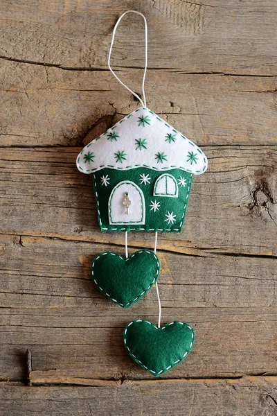 Green and white felt house Christmas tree ornament decorated with snowflakes and a small metal key. Happy holidays house with hearts decor isolated on rustic wood planks background. Wooden winter background Christmas house. Top view