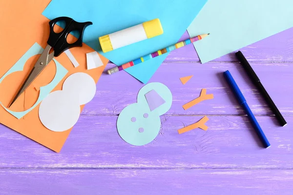 Making a children winter paper card. Step. Snowman parts cut from paper, scissors, markers, pencil, glue stick, colored paper set, snowman templates on wooden table. Kids winter DIY project. Top view — Stock Photo, Image