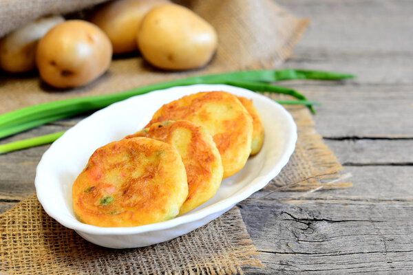Roasted vegetable cutlets. Potato cutlets with vegetables and spices on plate and on wooden table. Raw potatoes, fresh green onions. Vintage style. Closeup. Tasty vegetarian dish