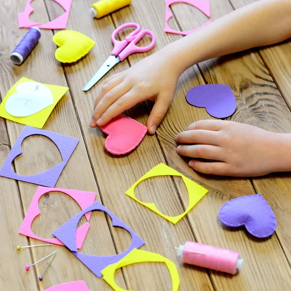 Kind gemaakt harten uit vilt. De handen van kinderen op tafel. Handgemaakte Valentines day hart geschenken, ambachten materialen en gereedschappen op een houten tafel. Aftelkalender voor Valentijnsdag ambachtelijke project — Stockfoto