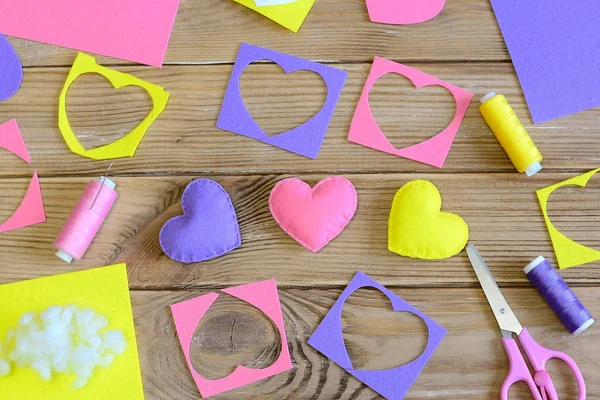 Valentine\'s day hearts crafts. Colorful hearts gifts made of felt, felt scraps, scissors, thread on wooden table. Valentine\'s day handmade gifts concept. Needlework background. Top view