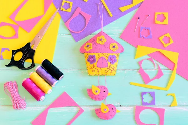 Felt wall hanging decoration. Spring felt toy house diy with birds and flowers, scissors, thread spool, colored felt sheets and scraps on a wooden table. Handmade work gift projects by children. Sewing craft tools accessories flat lay — Stock Photo, Image
