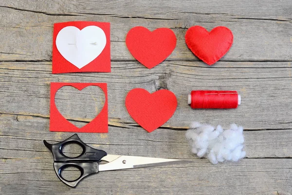 How to make a Valentine heart from a felt on Valentines Day. Sewing guide. Red felt heart, cut felt pieces in shape of a heart, paper template, scissors, thread, needle on a wooden table. Top view