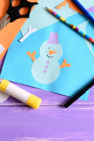 Маленький ребенок сделал бумажную открытку со снеговиком, снежинками и словами, которые я люблю зиму. Ножницы, клеевая палка, карандаш, маркеры, цветная бумага на деревянном столе. Детский бумажный фон. Крупный план — стоковое фото