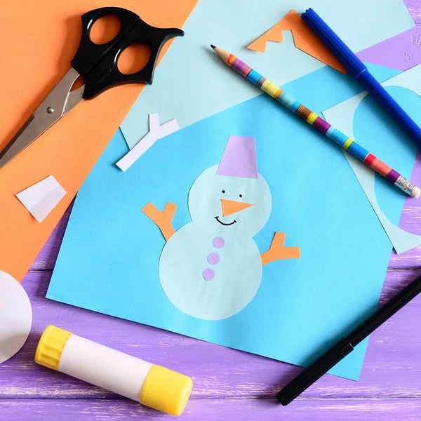 Kid made a paper card with a snowman, snowflakes and words I love winter. Scissors, glue stick, pencil, markers, colored paper sheets on a wooden table. Kids paper crafts. Closeup. Top view — Stock Photo, Image