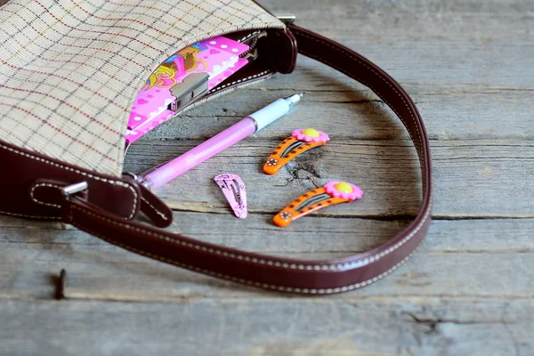 Kinderhandtasche und Accessoires auf Holztisch. kleine Handtasche, Notizbuch, rosa Stift, helle Haarspangen für Mädchen. Mädchen Handtasche Inhalt. Nahaufnahme — Stockfoto